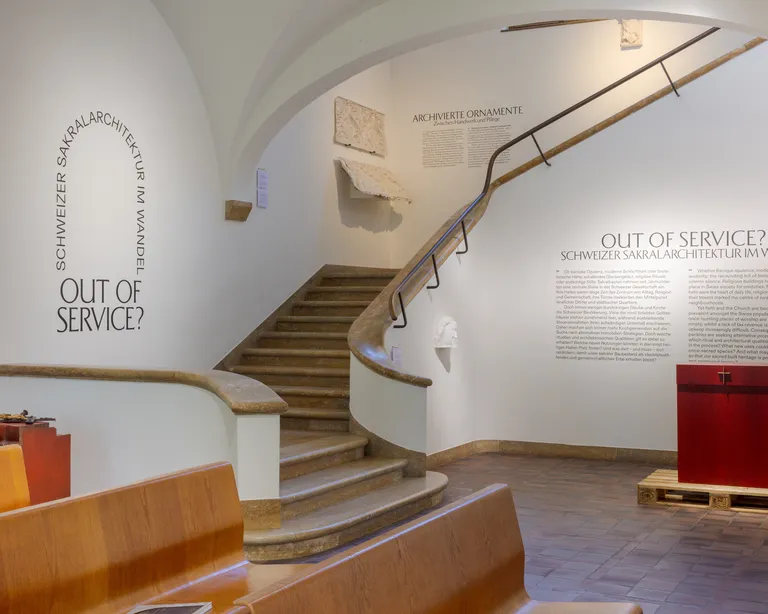 Heller Eingangsbereich eines Museums mit geschwungener Treppe, Infotafel an der Wand und einer Ausstellungsplattform.