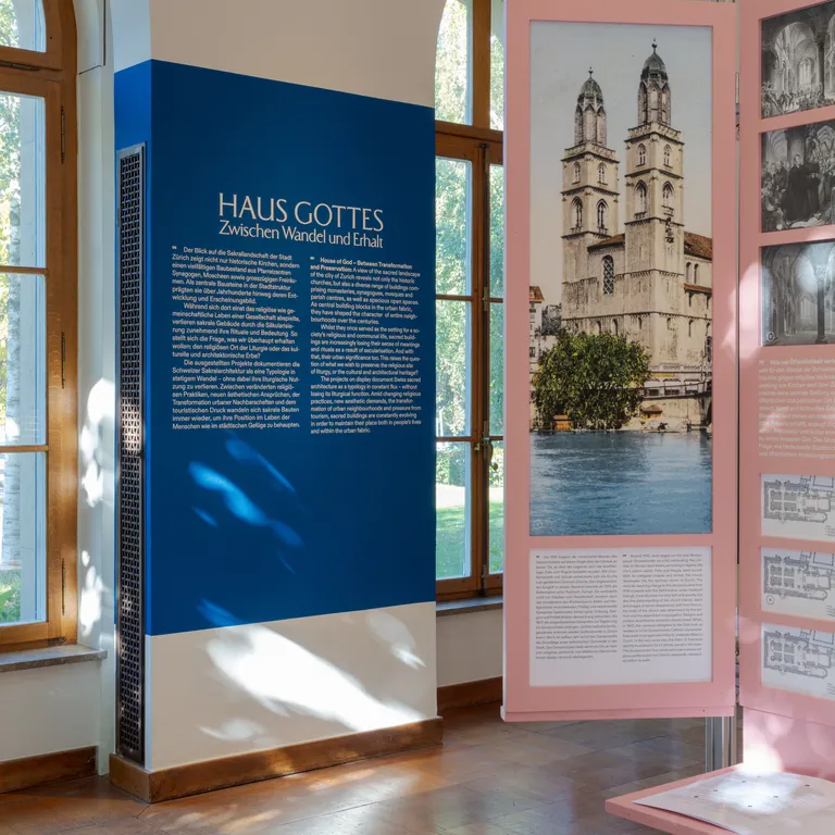 Alt-Text: Menschen tanzen auf einer runden Bühne in einem hellen Saal mit großen Fenstern, Zuschauer sitzen im Halbkreis.