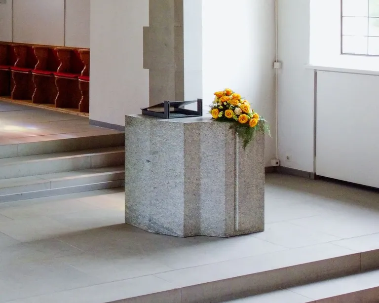 Sechseckiges Taufbecken aus Stein mit Blumenstrauss auf der Seite in der hellen Kirche Höngg.
