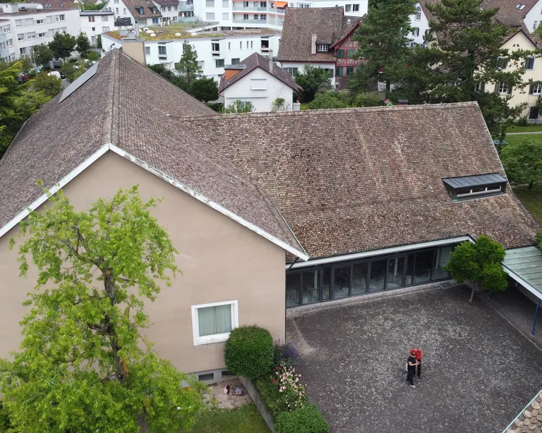 Luftaufnahme des Kirchgemeindehaus Höngg, umgeben von Bäumen und weiteren Gebäuden im Hintergrund.