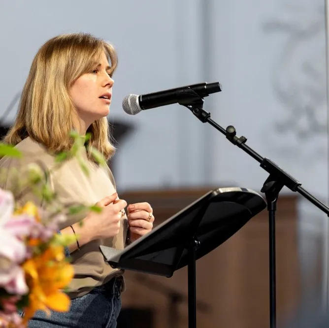 Franka Feder, unsere Community Managerin, spricht an einem Mikrofon auf einer Bühne, im Vordergrund ein bunter Blumenstrauß.