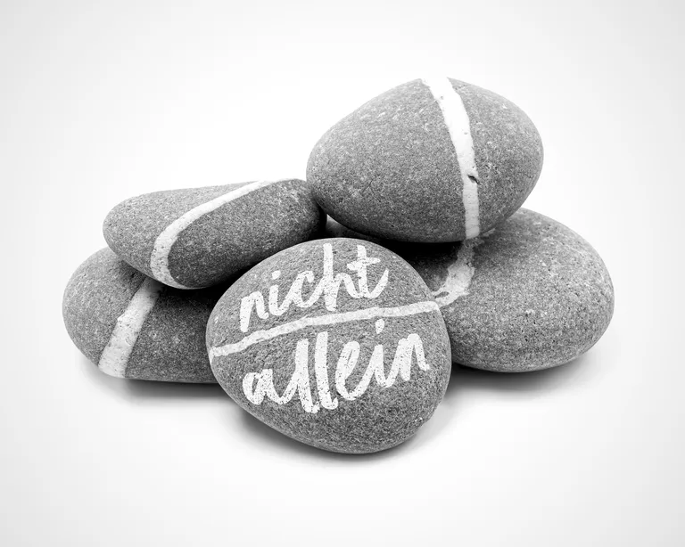 Fünf Steine, einer davon mit der Aufschrift «nicht allein», auf einem hellen Hintergrund gestapelt.