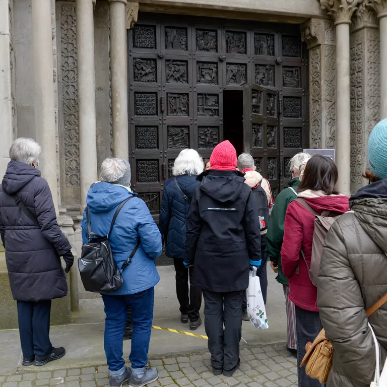 Eine Gruppe Menschen betritt die Kirche Grossmünster durch den Haupteingang.