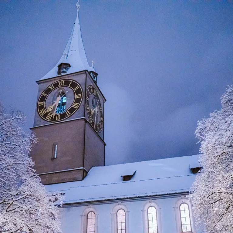St. Peter im Winter, Schnee bedeckt Dach und Bäume, blauer Abendhimmel im Hintergrund.