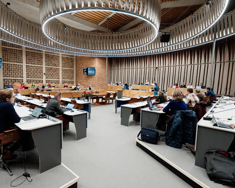 Menschen sitzen in einem modernen, runden Konferenzraum an Tischen und nehmen an einer Besprechung teil.