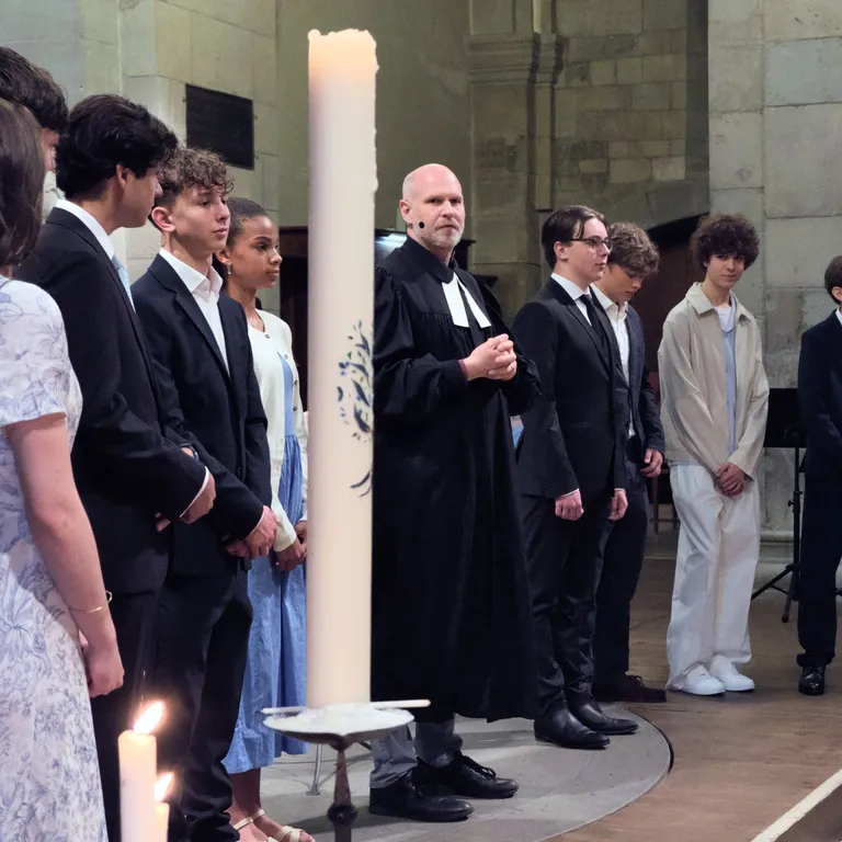 Mehrere Jugendliche und ein Pfarrer stehen neben einer großen Kerze in einer Kirche, alle festlich gekleidet.