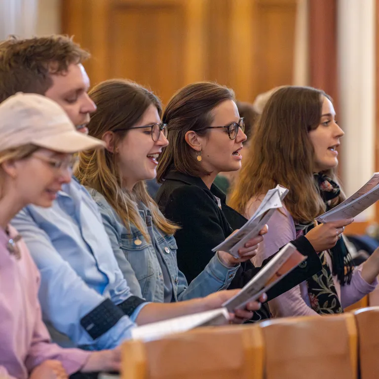 Mehrere junge Menschen sitzen in einer Reihe in einer Kirche und singen gemeinsam aus Liederbüchern.