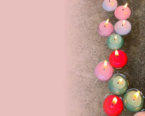 Mehrere bunte, brennende Teelichter stehen auf einem grauen Untergrund, links daneben eine rosa Fläche.