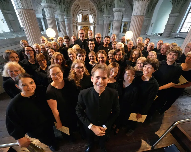 Eine große Chorgruppe in schwarzer Kleidung steht in einer Kirche und blickt lächelnd in die Kamera.