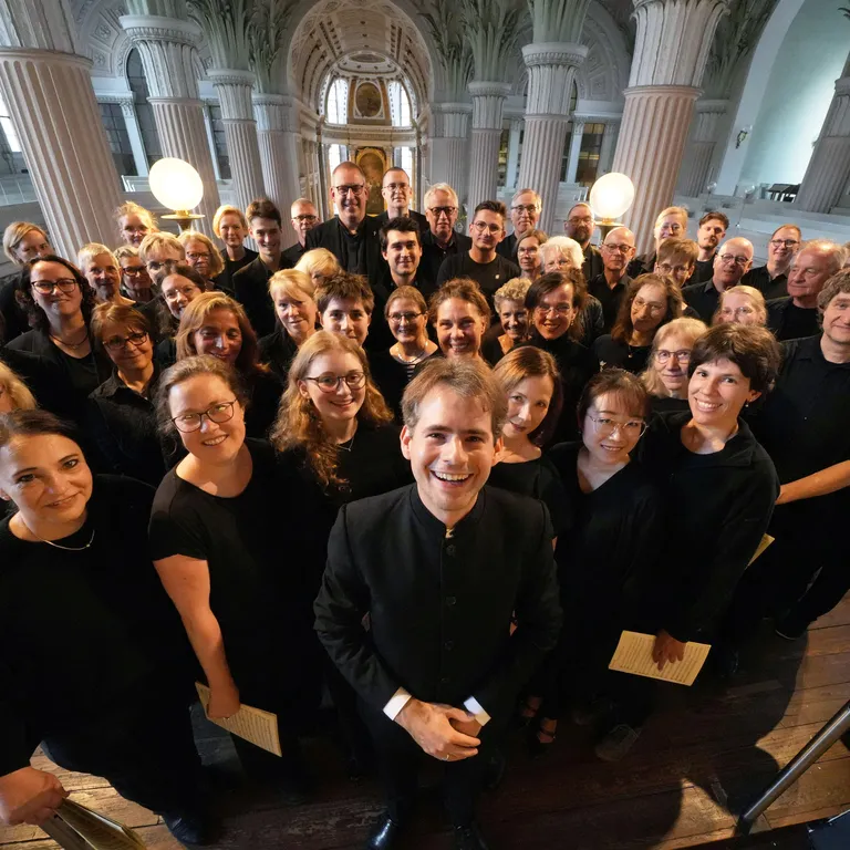Eine große Chorgruppe in schwarzer Kleidung steht in einer Kirche und blickt lächelnd in die Kamera.