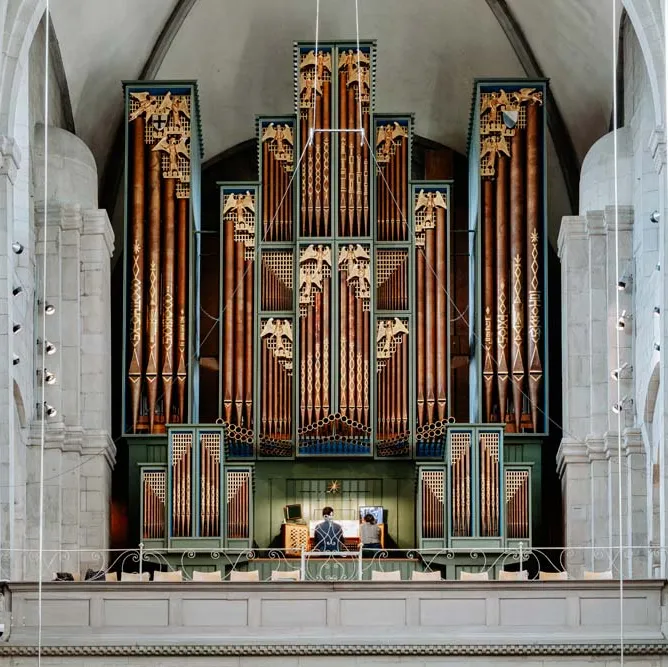 Grosse Orgel im Grossmünster, Personen sitzen unten an der Empore, hohe weisse Gewölbedecke.