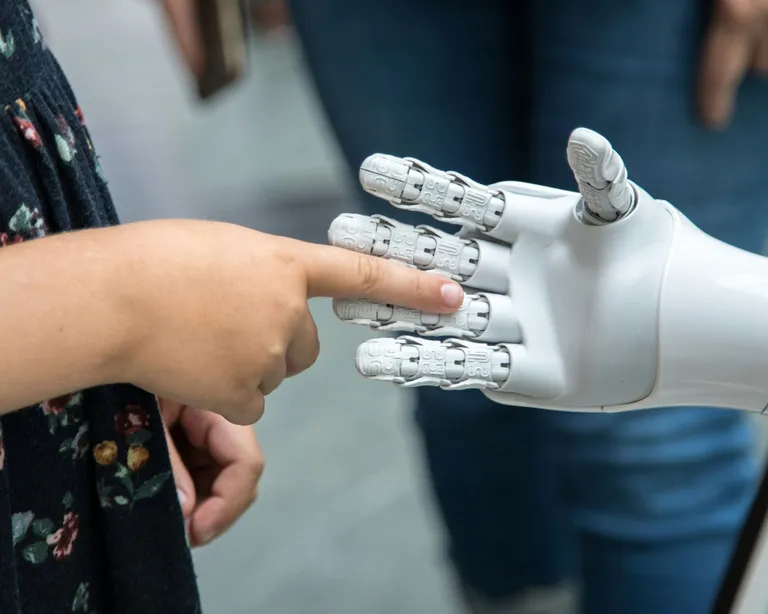 Ein Kind berührt mit dem Finger die Hand eines Roboters, Hintergrund unscharf.