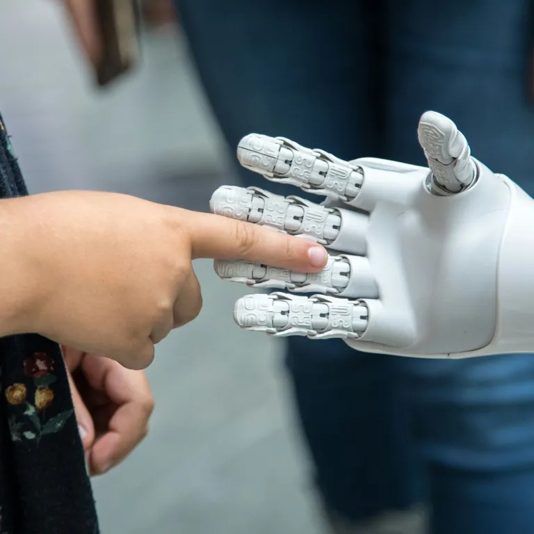 Ein Kind berührt mit dem Finger die Hand eines Roboters, Hintergrund unscharf.