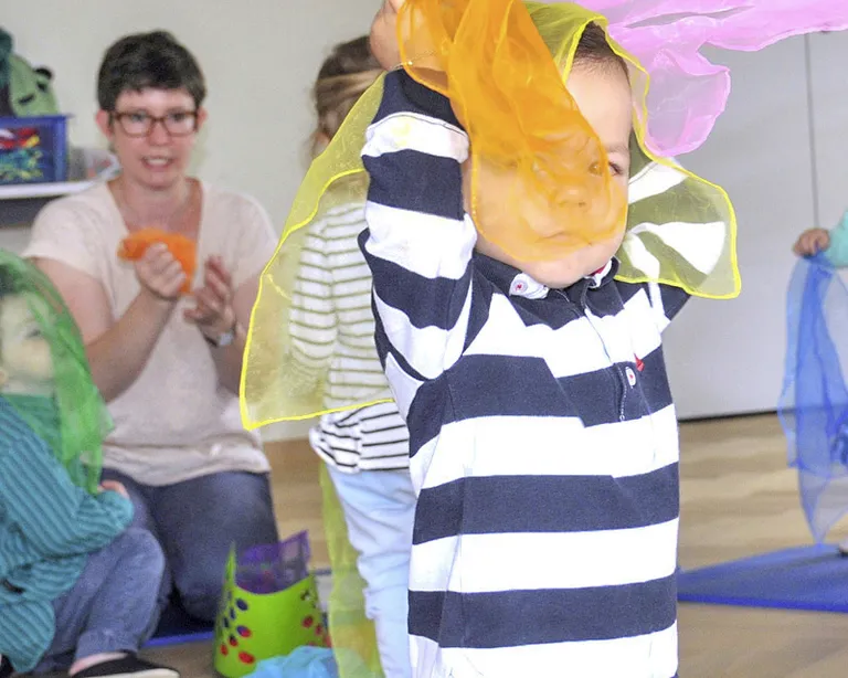 Mehrere Kinder und Erwachsene spielen gemeinsam im Singe mit de Chinde, einige tragen bunte Tücher.