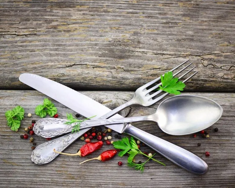 Drei Besteckteile auf Holz, dekoriert mit Kräutern, roten Chilis und Pfefferkörnern.