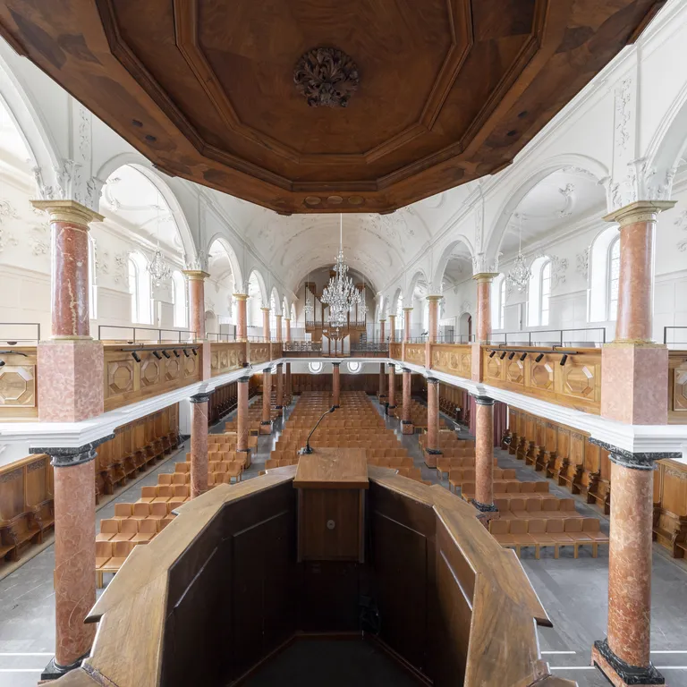 Heller, klassischer Kirchenraum mit Holzkanzel, Emporen, steinernen Säulen und großen Rundbogenfenstern.