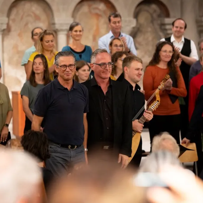 Die beiden Kantoren vom Grossmünster Roman Walker und Sacha Rüegg stehen inmitten eines Orchesters im Grossmünster.