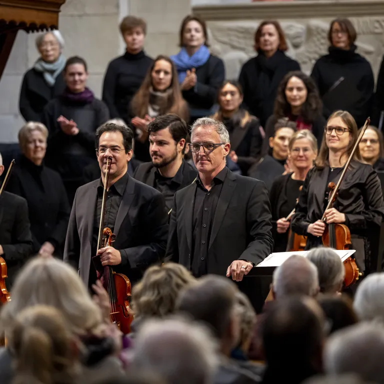 Ein Orchester und Chor stehen nach einem Konzert in einer Kirche vor Publikum und lächeln.