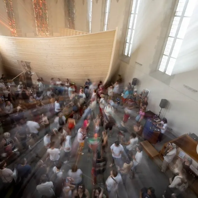 Viele Menschen sitzen und stehen in einer hellen Kirche mit großen Fenstern und Orgel, aufgenommen aus der Vogelperspektive.