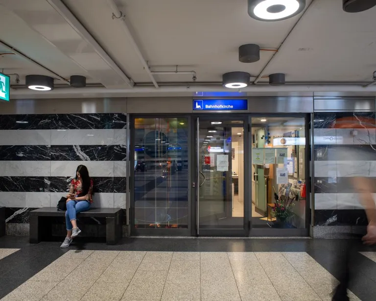 Eine Frau sitzt auf einer Bank in einer modernen U-Bahn-Station vor einem geschlossenen Geschäft.