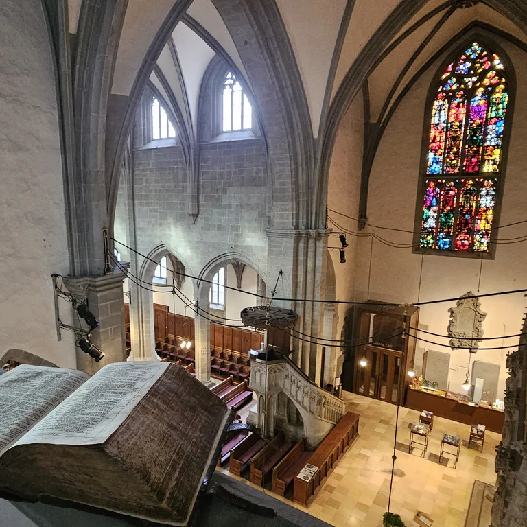Aufgeschlagene alte Bibel auf einem Balkon in der Kirche Fraumünster mit bunten Kirchenfenster im Hintergrund und Blick auf die Kanzel.