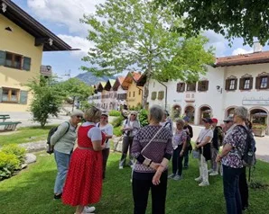 Eine Gruppe von Menschen steht auf einer Wiese im Dorf, umgeben von traditionellen Häusern und Bäumen.