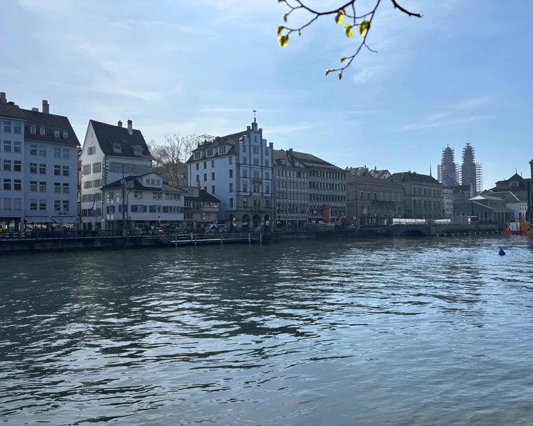 Häuser am Flussufer bei Tageslicht, im Hintergrund Kirchtürme und blauer Himmel. Ein Symbolbild für die Spuren der Reformation.