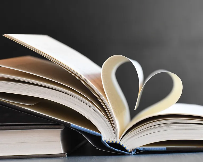 Ein aufgeschlagenes Buch, dessen Seiten ein Herz formen, liegt vor dunklem Hintergrund.