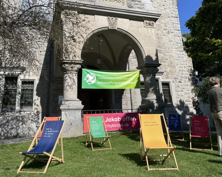 Mehrere bunte Liegestühle stehen auf dem Rasen vor der Citykirche mit einem grünen Banner am Eingang.