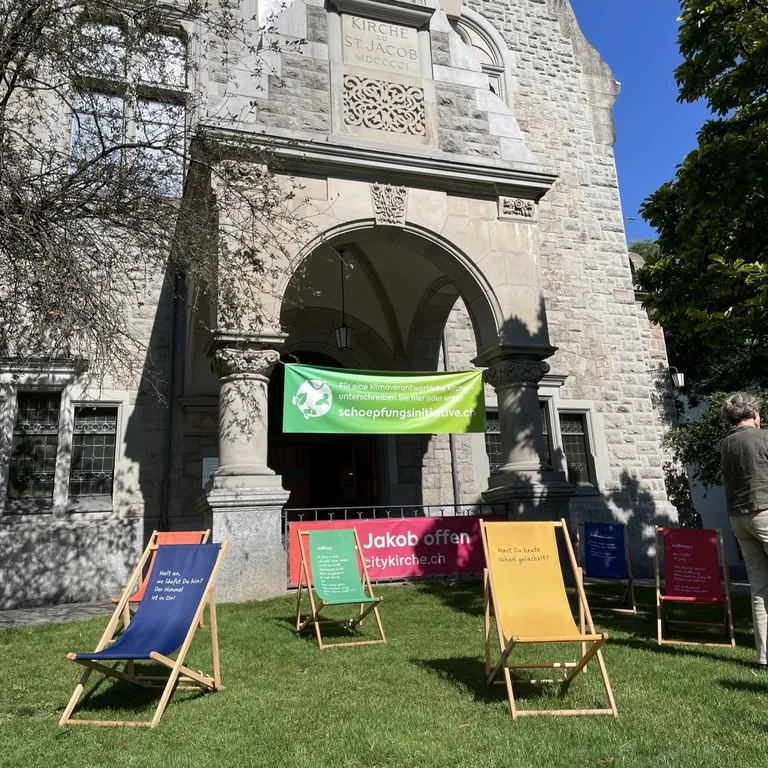 Mehrere bunte Liegestühle stehen auf dem Rasen vor der Citykirche mit einem grünen Banner am Eingang.