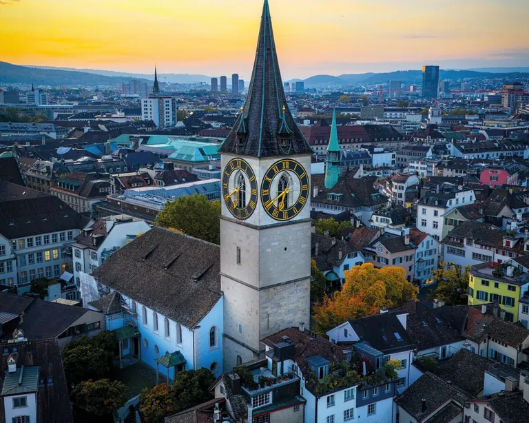 Kirchturm der Kirche St. Peter, umgeben von Stadtgebäuden bei Sonnenuntergang.