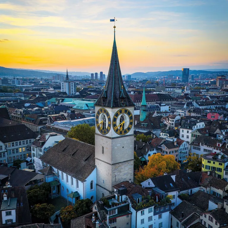Kirchturm der Kirche St. Peter, umgeben von Stadtgebäuden bei Sonnenuntergang.