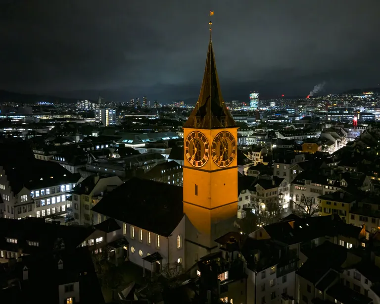 Turm der Stadtkirche St. Peter in Zürich leuchtet orange in der Abenddämmerung.