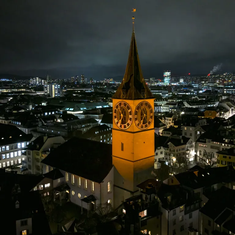 Turm der Stadtkirche St. Peter in Zürich leuchtet orange in der Abenddämmerung.