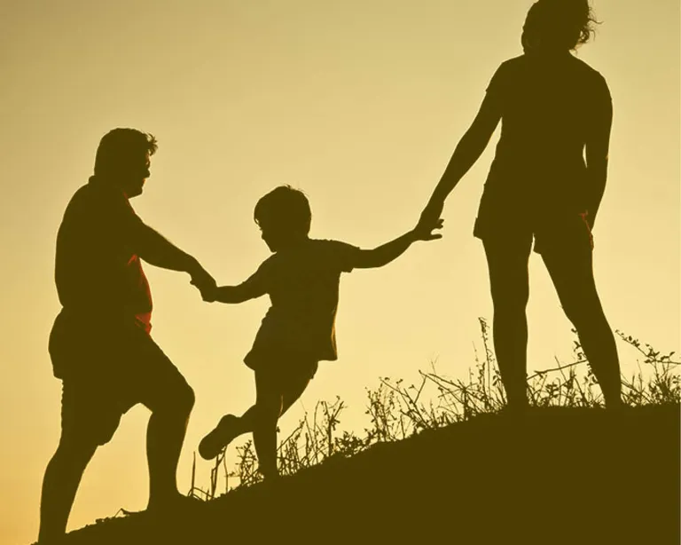 Silhouette von drei Personen, die sich an den Händen halten und gemeinsam einen Hügel bei Sonnenuntergang hinaufgehen.