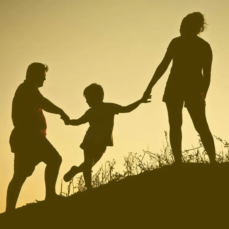 Silhouette von drei Personen, die sich an den Händen halten und gemeinsam einen Hügel bei Sonnenuntergang hinaufgehen.