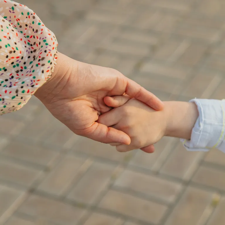 Eine erwachsene und eine Kinderhand halten sich auf einem gepflasterten Untergrund.