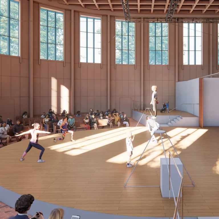 Alt-Text: Menschen tanzen auf einer runden Bühne in einem hellen Saal mit großen Fenstern, Zuschauer sitzen im Halbkreis.