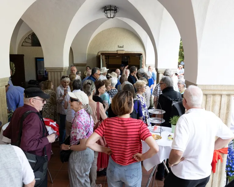 Eine Gruppe Menschen steht unter der Arkade der Kirche Neumünster bei einem Apero