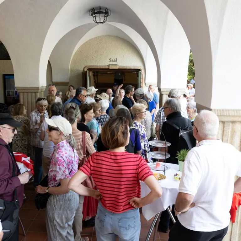 Eine Gruppe Menschen steht unter der Arkade der Kirche Neumünster bei einem Apero