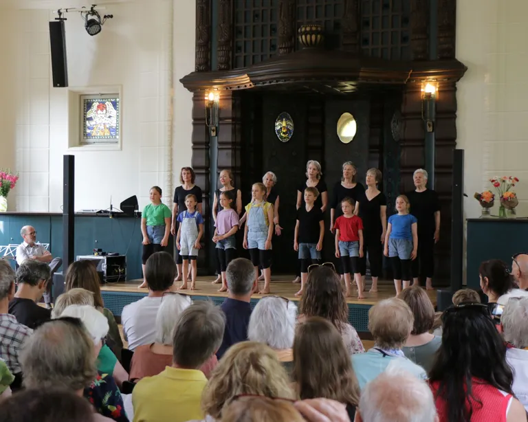 Erwachsene und Kinder stehen vor einem Publikum auf einer Bühne während eines Gottesdienstes