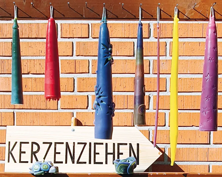 Selbstgemachte Kerzen hängen vor einer Backstein-Wand, unten ein Schild mit dem Wort Kerzenziehen