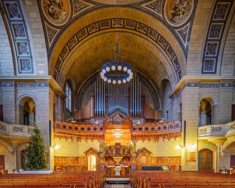 Innenraum einer prunkvoll verzierten Kirche mit Holzbänken, Altar und bemalter Kuppeldecke.