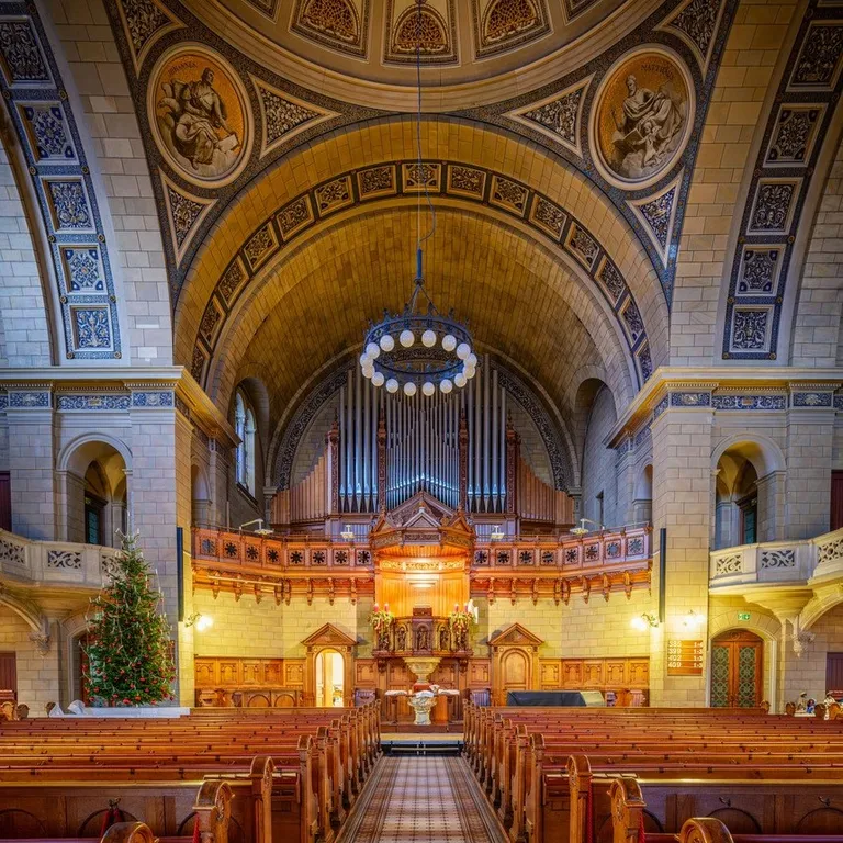 Innenraum einer prunkvoll verzierten Kirche mit Holzbänken, Altar und bemalter Kuppeldecke.