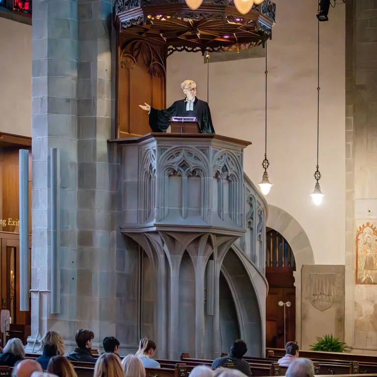 Ein Prediger steht auf der Kanzel einer Kirche, während die Gemeinde in den Bänken zuhört.