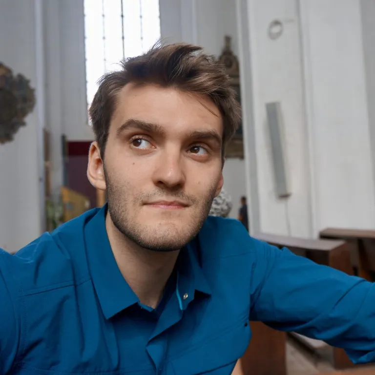 Junger Mann in blauem Hemd sitzt nachdenklich in einer hellen, modernen Kirche auf einer Bank.