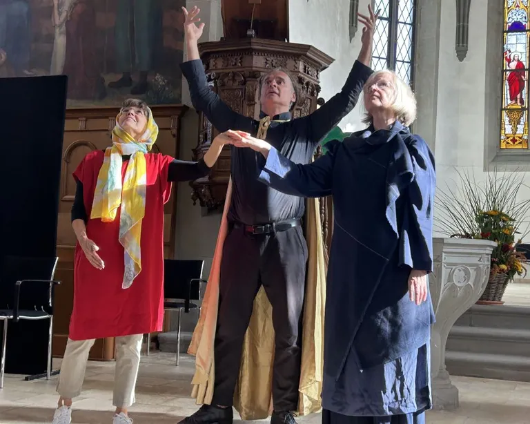 Drei Personen stehen in der Kirche, Hände in die Luft gestreckt und nach oben schauend