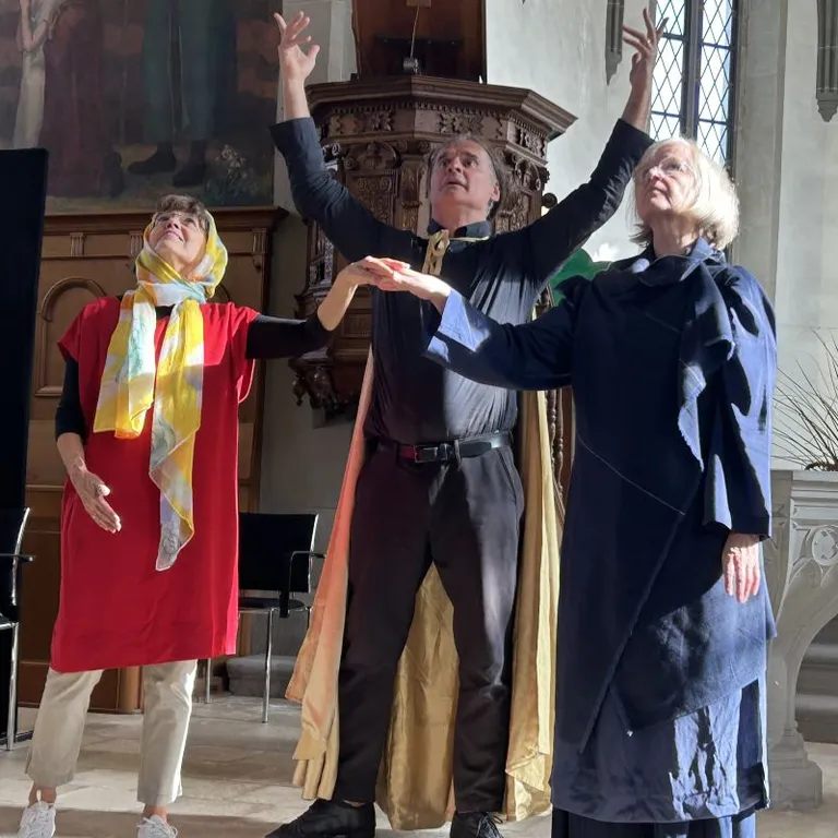 Drei Personen stehen in der Kirche, Hände in die Luft gestreckt und nach oben schauend