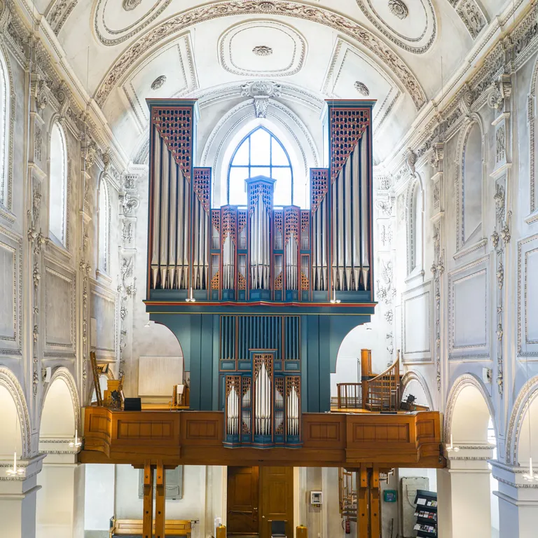Blick in das helle Kirchenschiff mit hölzernen Bänken und einer großen Orgel auf der Empore im Hintergrund.