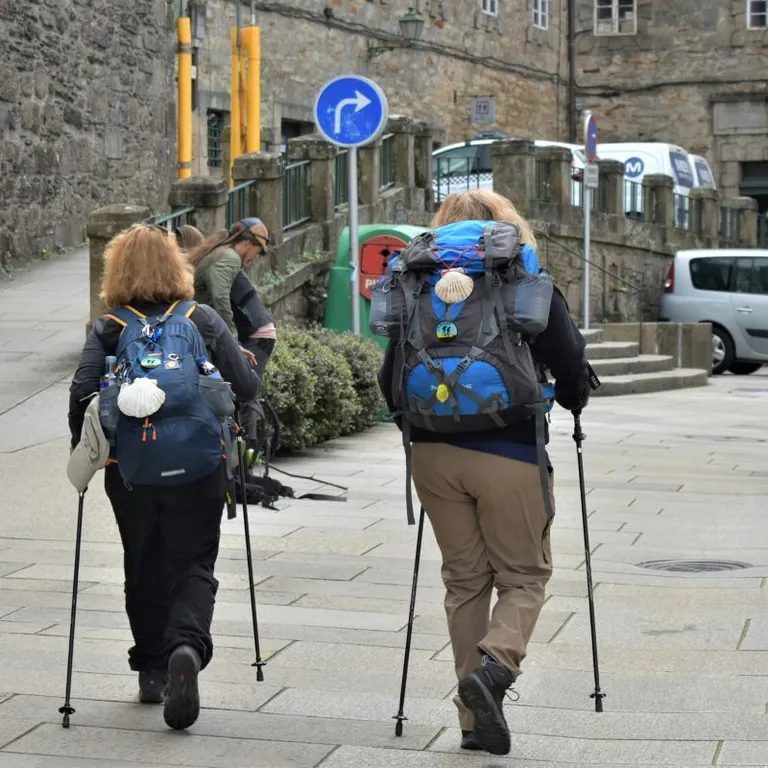 Zwei Wanderer mit grossen Rucksäcken und Stöcken gehen durch eine gepflasterte Stadtstrasse.